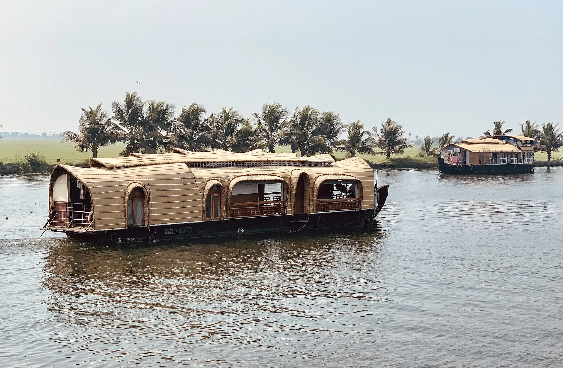 A thatched-roof houseboat gliding on calm backwaters lined with coconut palms